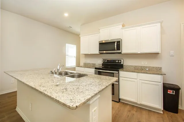 a kitchen with kitchen island granite countertop a sink appliances cabinets and wooden floor