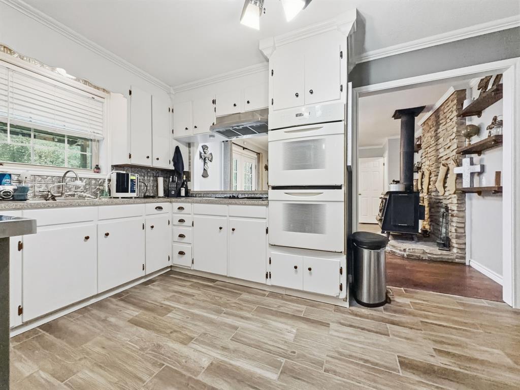 206 Navajo Trail Hamilton, TX 76531 - Photo 9 of 39 Kitchen featuring double oven, a wood stove, white cabinets, plenty of natural light, and ornamental molding