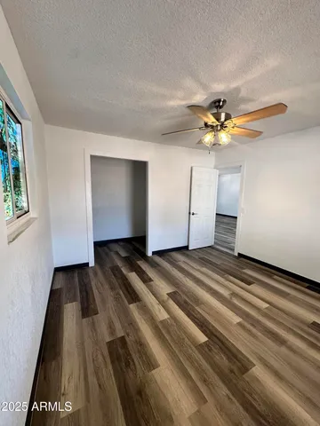 a view of an empty room with chandelier fan and wooden floor