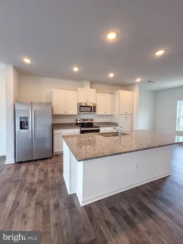 a kitchen with granite countertop a refrigerator a stove and a sink with wooden floors