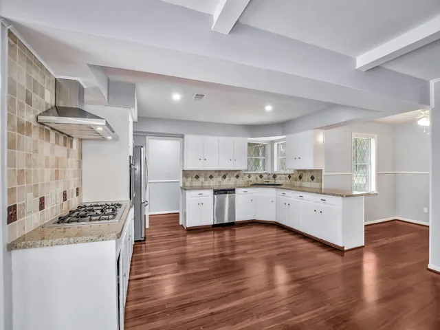 a large kitchen with stainless steel appliances kitchen island a stove a sink dishwasher a refrigerator white cabinets and wooden floor