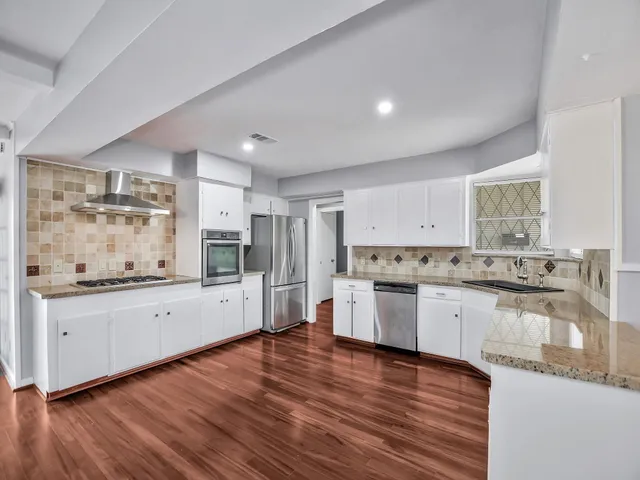 a large kitchen with granite countertop a stove top oven a sink a counter space and wooden floor