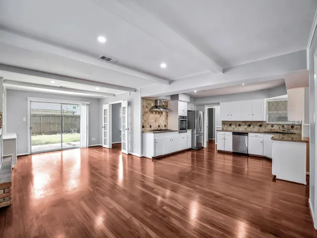 a view of an empty room and kitchen with wooden floor
