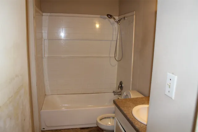 a bathroom with a granite countertop bathtub shower sink vanity and toilet