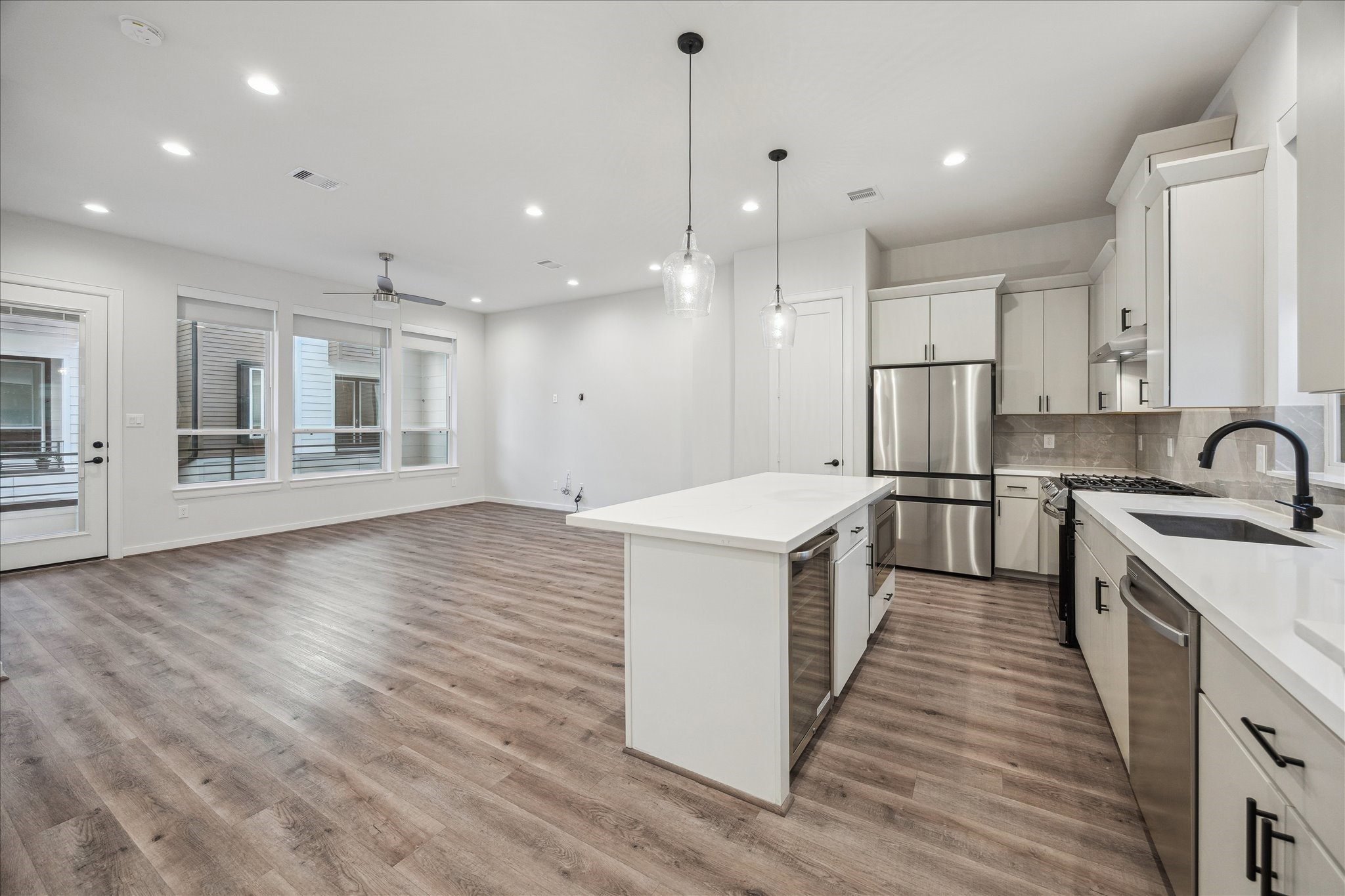 1603 Patterson Street, Unit E Houston, TX 77007 - Photo 14 of 32 This modern open-concept kitchen and living area features sleek wood flooring, abundant natural light from large windows, and stylish pendant lighting. The kitchen is equipped with stainless steel appliances, a central island, and ample cabinet space, creating a clean and inviting atmosphere perfect for entertaining.