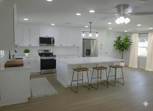 a kitchen with kitchen island stainless steel appliances a sink a stove a microwave a refrigerator and cabinets