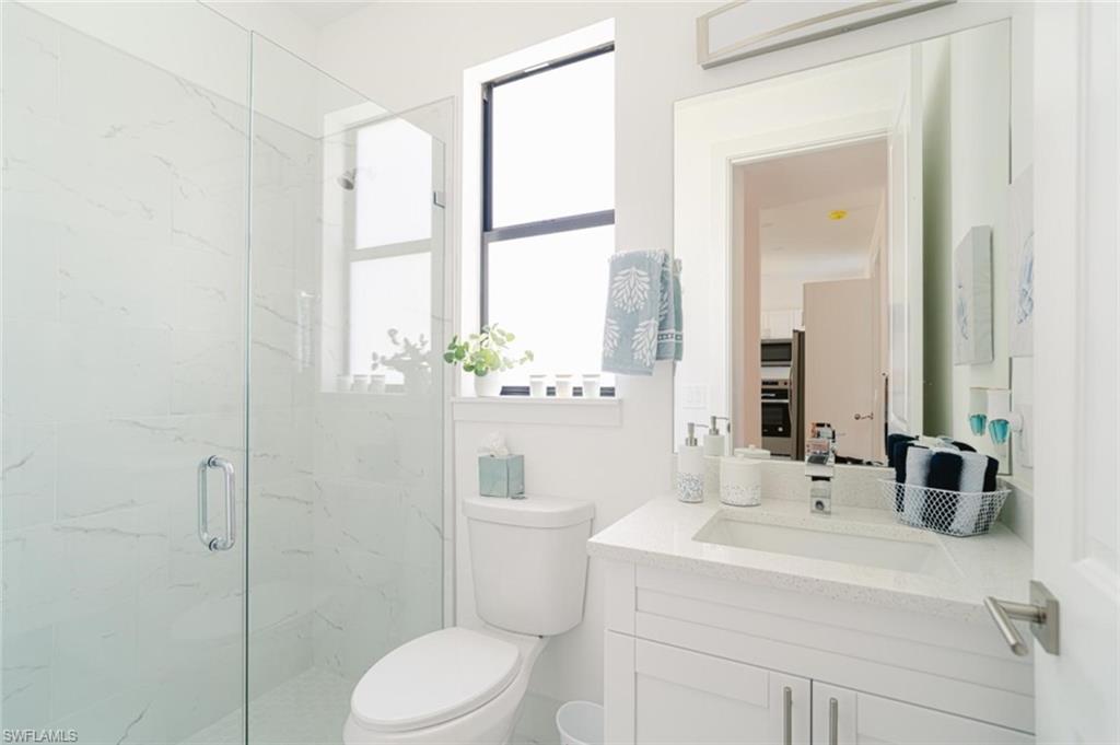 907 Homestead Road South Lehigh Acres, FL 33974 - Photo 28 of 43 Bathroom featuring a glass-enclosed shower with white marble-patterned tile, a white vanity with an integrated sink and light-colored countertop, and a large wall-mounted mirror