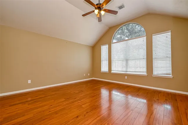 an empty room with wooden floor fan and windows