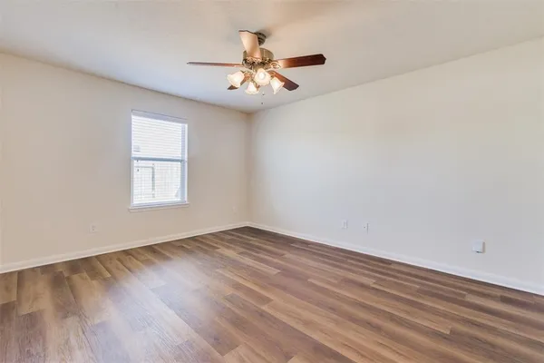 an empty room with wooden floor chandelier fan and windows