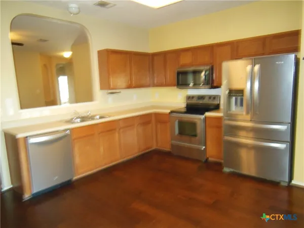 a kitchen with stainless steel appliances granite countertop a refrigerator a stove and a sink with wooden floor