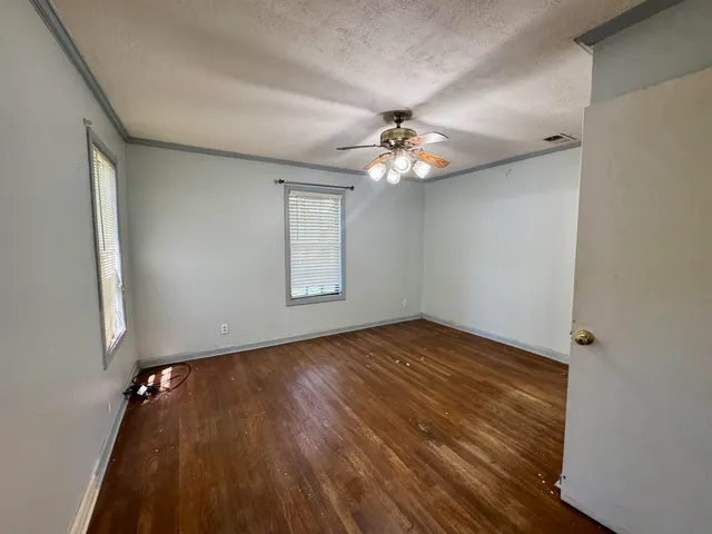 an empty room with wooden floor chandelier fan and windows