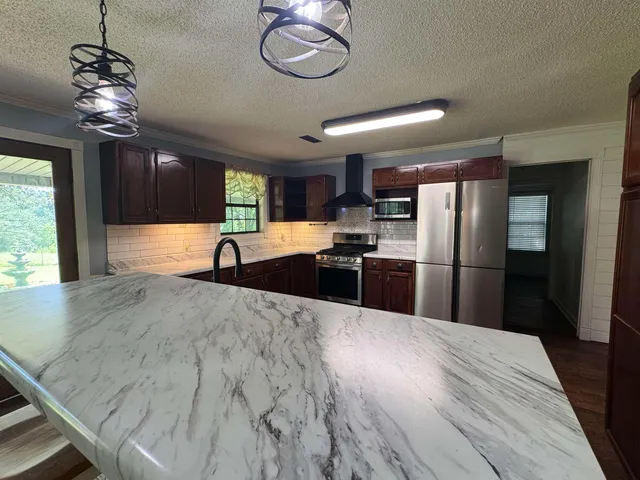 a large kitchen with stainless steel appliances granite countertop a refrigerator a sink dishwasher a stove and a dining table with wooden floor