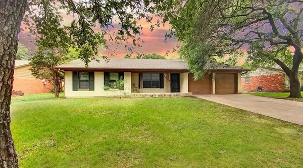 a view of a white house with a large tree and wooden fence