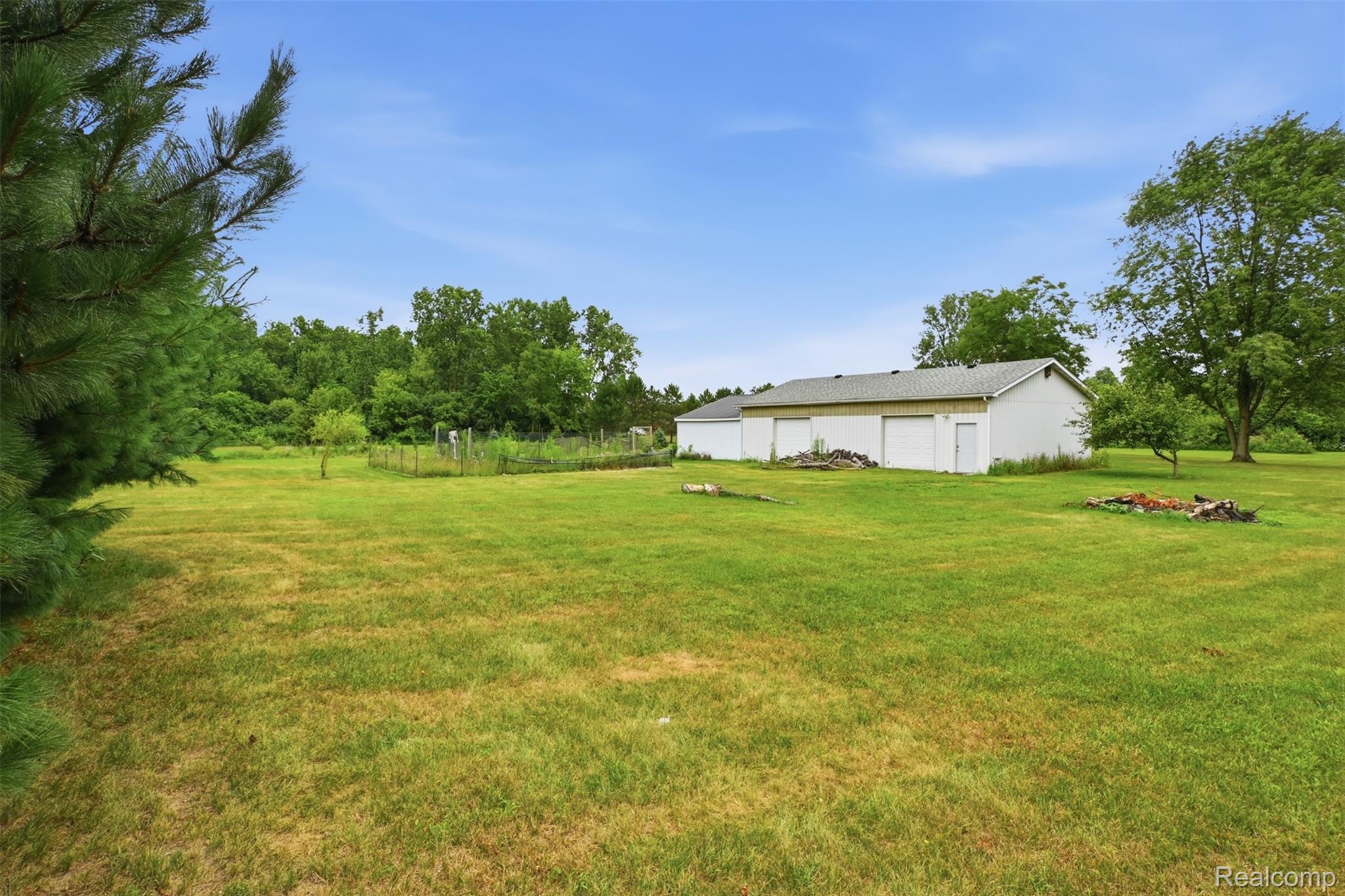 45738 Bemis Road Belleville, MI 48111 - Photo 44 of 52 Expansive grassy yard with perimeter trees, a white outbuilding featuring multiple garage doors, and a garden area