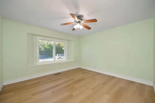 a view of an empty room with wooden floor and a ceiling fan