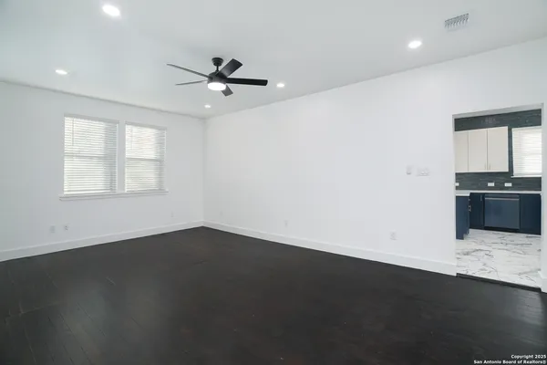 an empty room with wooden floor ceiling fan and windows