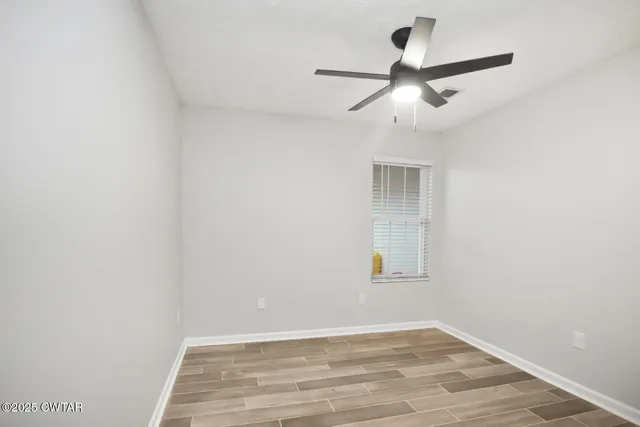 an empty room with wooden floor ceiling fan and windows
