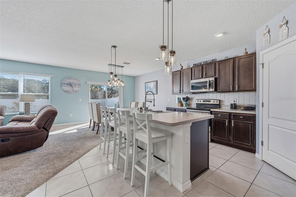 1526 White Hawk Way Groveland, FL 34736 - Photo 11 of 40 a kitchen with stainless steel appliances granite countertop a stove top oven a refrigerator a kitchen island a dining table and chairs with wooden floor