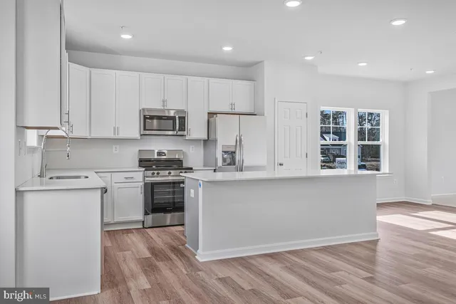 a large kitchen with kitchen island white cabinets wooden floor and stainless steel appliances