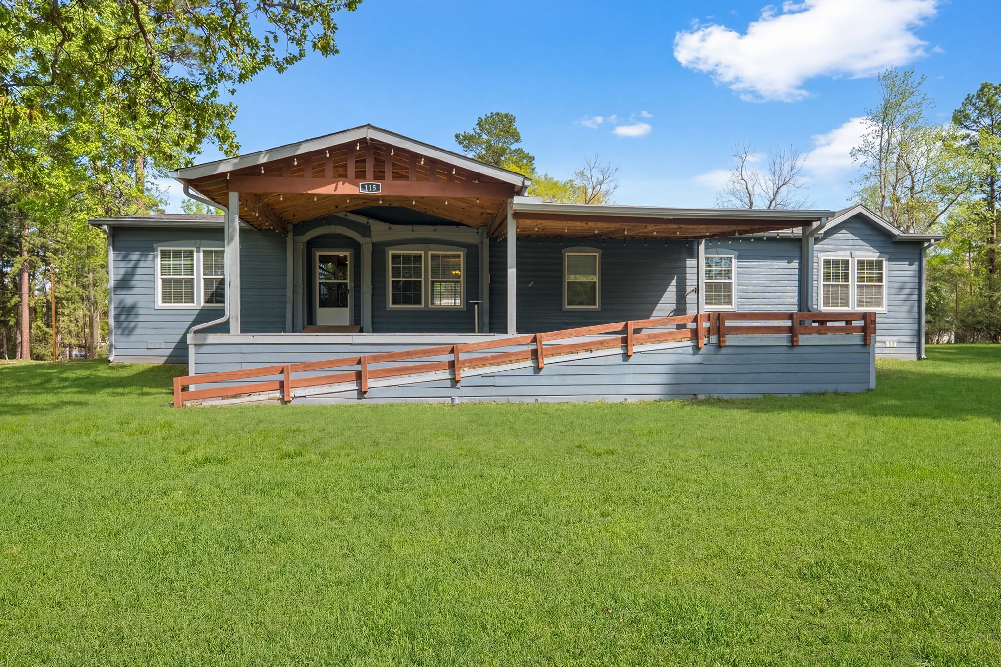115 Canadian Drive Trinity, TX 75862 - Photo 2 of 41 Charming single-story blue house with a welcoming front porch, ramp access, and surrounded by lush greenery, perfect for enjoying nature.