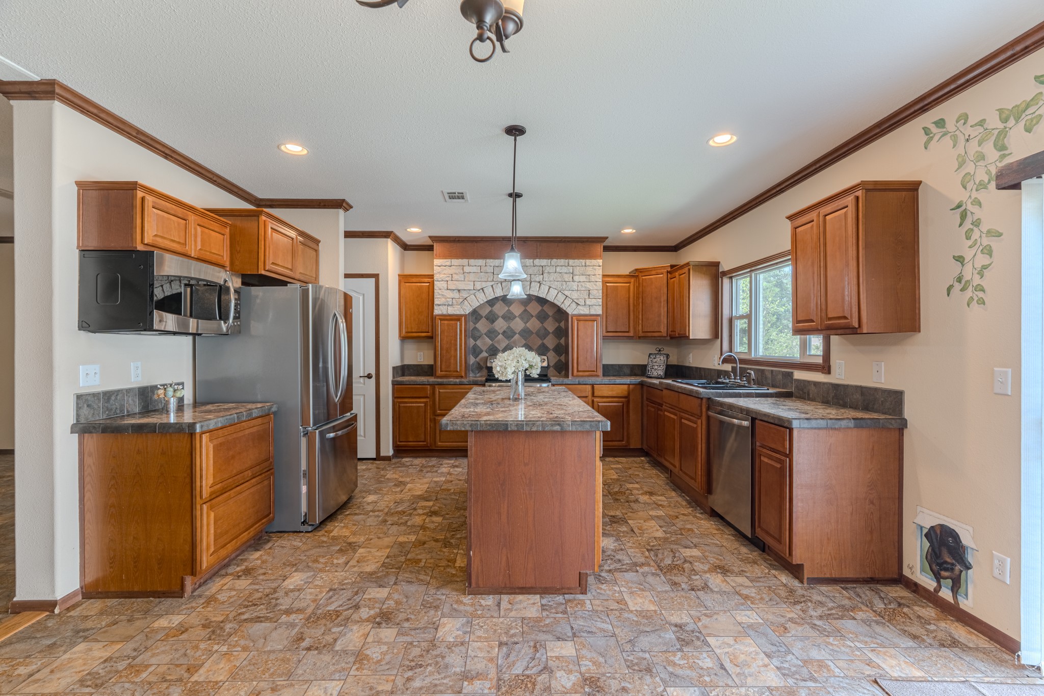 115 Canadian Drive Trinity, TX 75862 - Photo 7 of 41 Kitchen features warm wooden cabinetry, granite countertops, and a central island. It includes stainless steel appliances, ample natural light from large windows, and a decorative tile backsplash for a modern touch.
