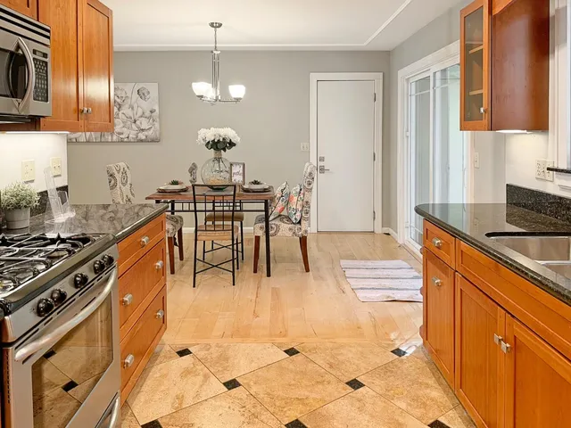 a kitchen with stainless steel appliances granite countertop a stove top oven a sink a dining table and chairs with wooden floor