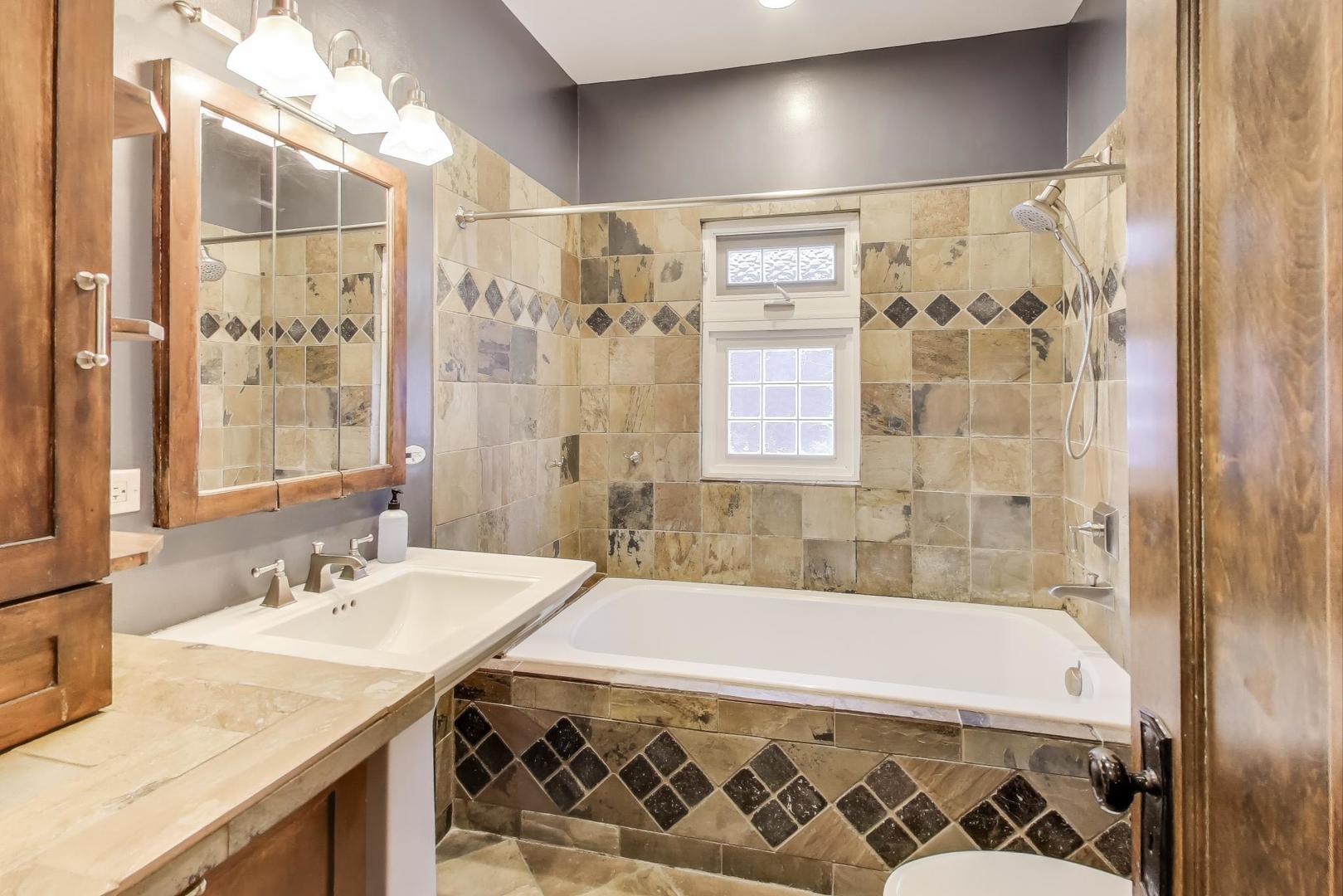 1020 Harvard Terrace Evanston, IL 60202 - Photo 18 of 31 a bathroom with a granite countertop sink a mirror a bathtub and shower