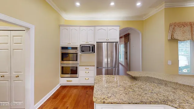 a large white kitchen with stainless steel appliances granite countertop a stove a sink dishwasher and cabinets with wooden floor