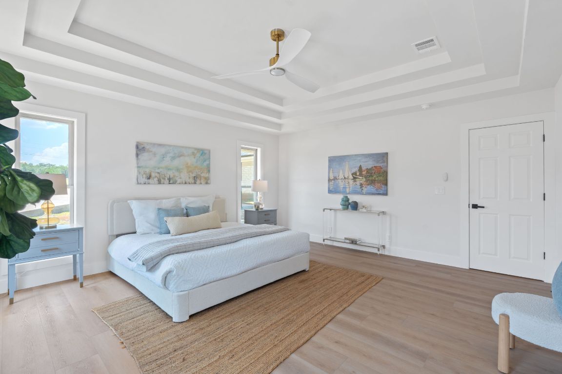 1325 Likeness Road Spicewood, TX 78669 - Photo 12 of 38 Bedroom with a tray ceiling, light wood-type flooring, and a ceiling fan