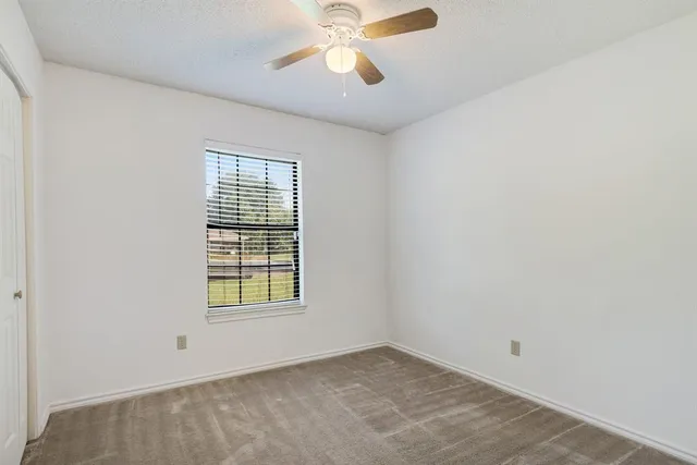 an empty room with chandelier fan and windows