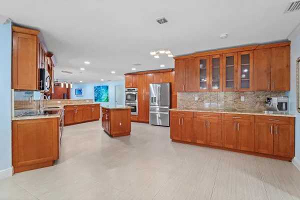 a large kitchen with stainless steel appliances kitchen island granite countertop a refrigerator and a stove top oven