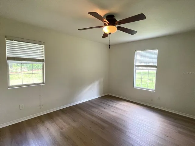 an empty room with wooden floor fan and windows