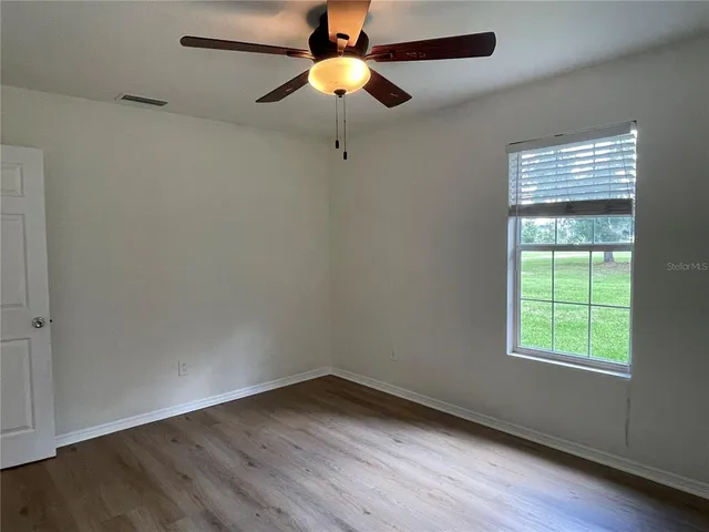 an empty room with wooden floor chandelier fan and windows
