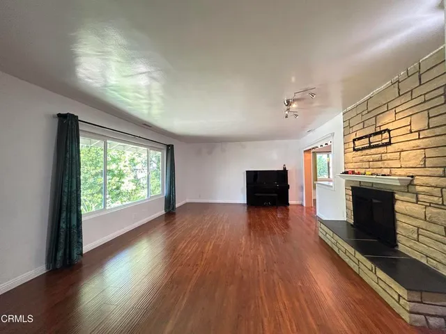 an empty room with wooden floor fireplace and windows