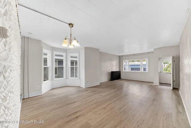an empty room with wooden floor chandelier and windows
