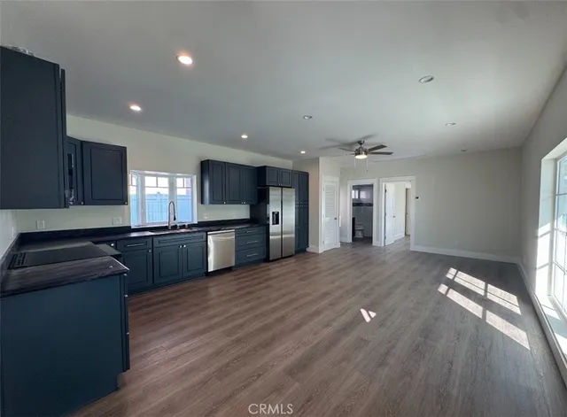 a kitchen with stainless steel appliances granite countertop a refrigerator a sink dishwasher a stove and white countertops with wooden floor