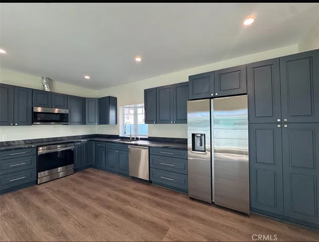 a large kitchen with stainless steel appliances granite countertop a refrigerator a sink dishwasher a stove with wooden cabinets and floor