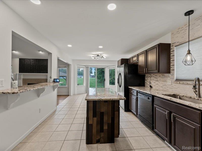 29213 Rachid Lane New Baltimore, MI 48047 - Photo 8 of 26 Kitchen featuring light stone countertops, dark wood finish cabinets, a center island, light tile patterned floors, and a fireplace