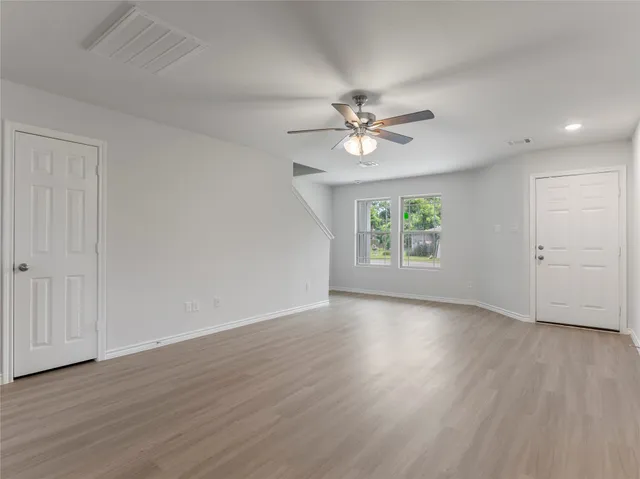 an empty room with wooden floor chandelier fan and windows