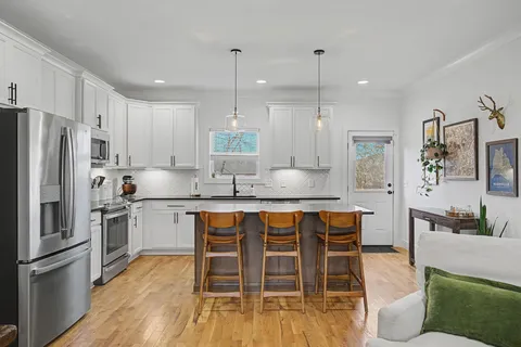 a kitchen with stainless steel appliances granite countertop a stove a sink a refrigerator and a dining table with wooden floor