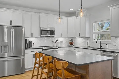 a kitchen with stainless steel appliances granite countertop a refrigerator a sink dishwasher a stove and white cabinets with wooden floor