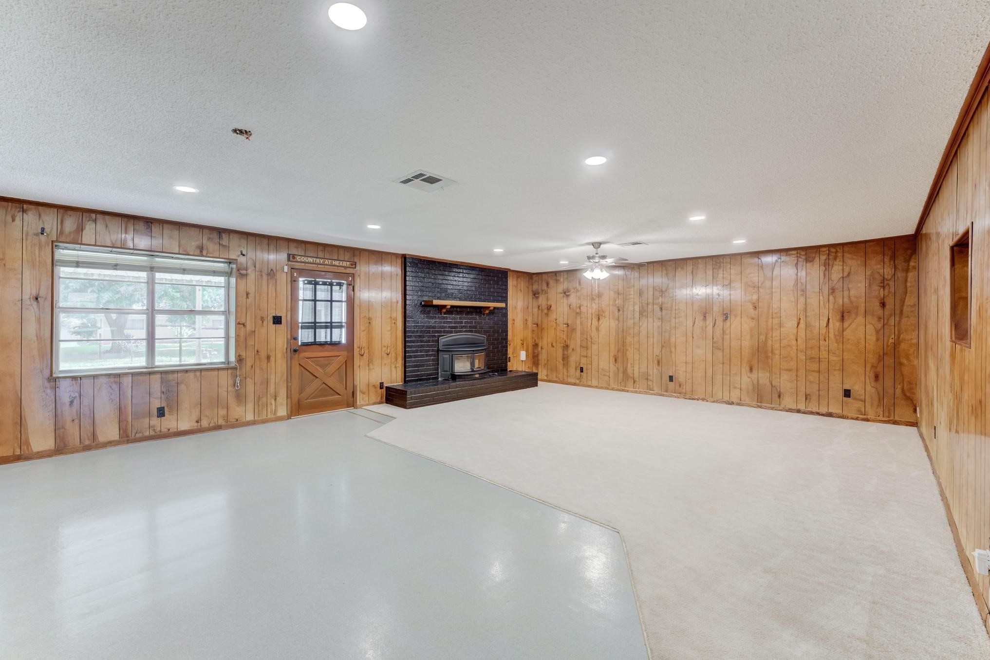 305 Yaupon Street Sweeny, TX 77480 - Photo 1 of 22 Spacious living room with wood paneling, a brick fireplace, ceiling fan, and large window. Cozy and inviting with ample natural light.