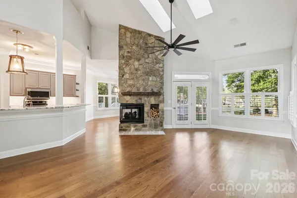 an empty room with wooden floor a fireplace a kitchen view and windows