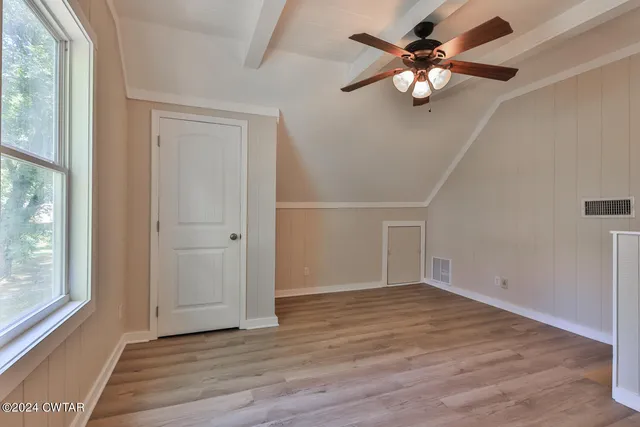 an empty room with wooden floor fan and windows