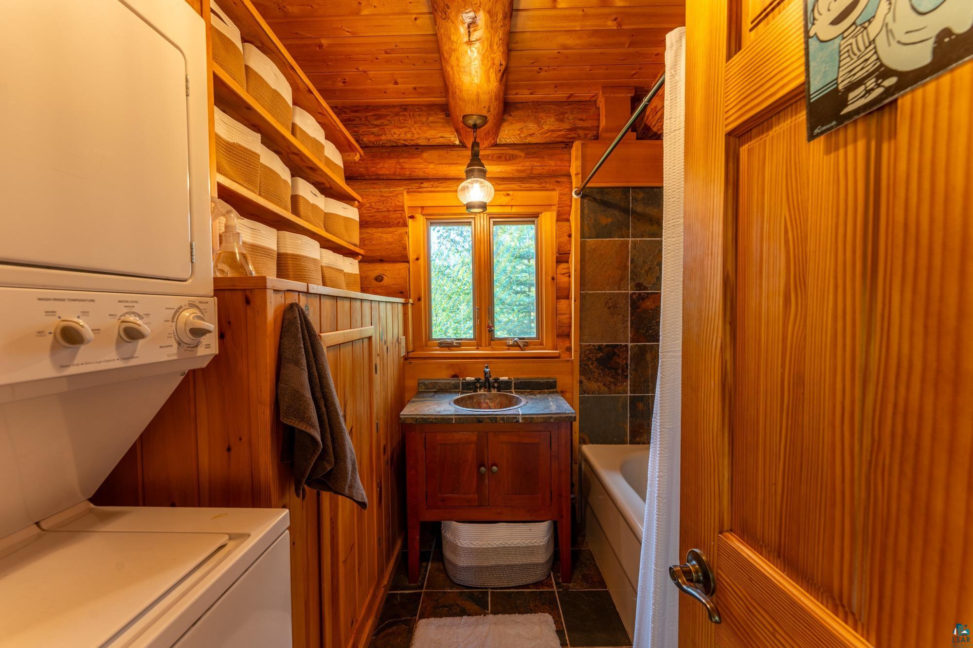 1911 Grouse Ridge Road Ely, MN 55731 - Photo 11 of 42 Washroom with log walls, dark tile patterned floors, wood ceiling, sink, and stacked washing maching and dryer