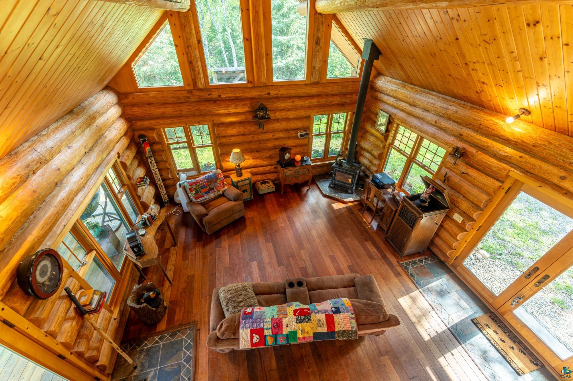 1911 Grouse Ridge Road Ely, MN 55731 - Photo 15 of 42 Living room featuring hardwood / wood-style flooring, a wood stove, high vaulted ceiling, and rustic walls
