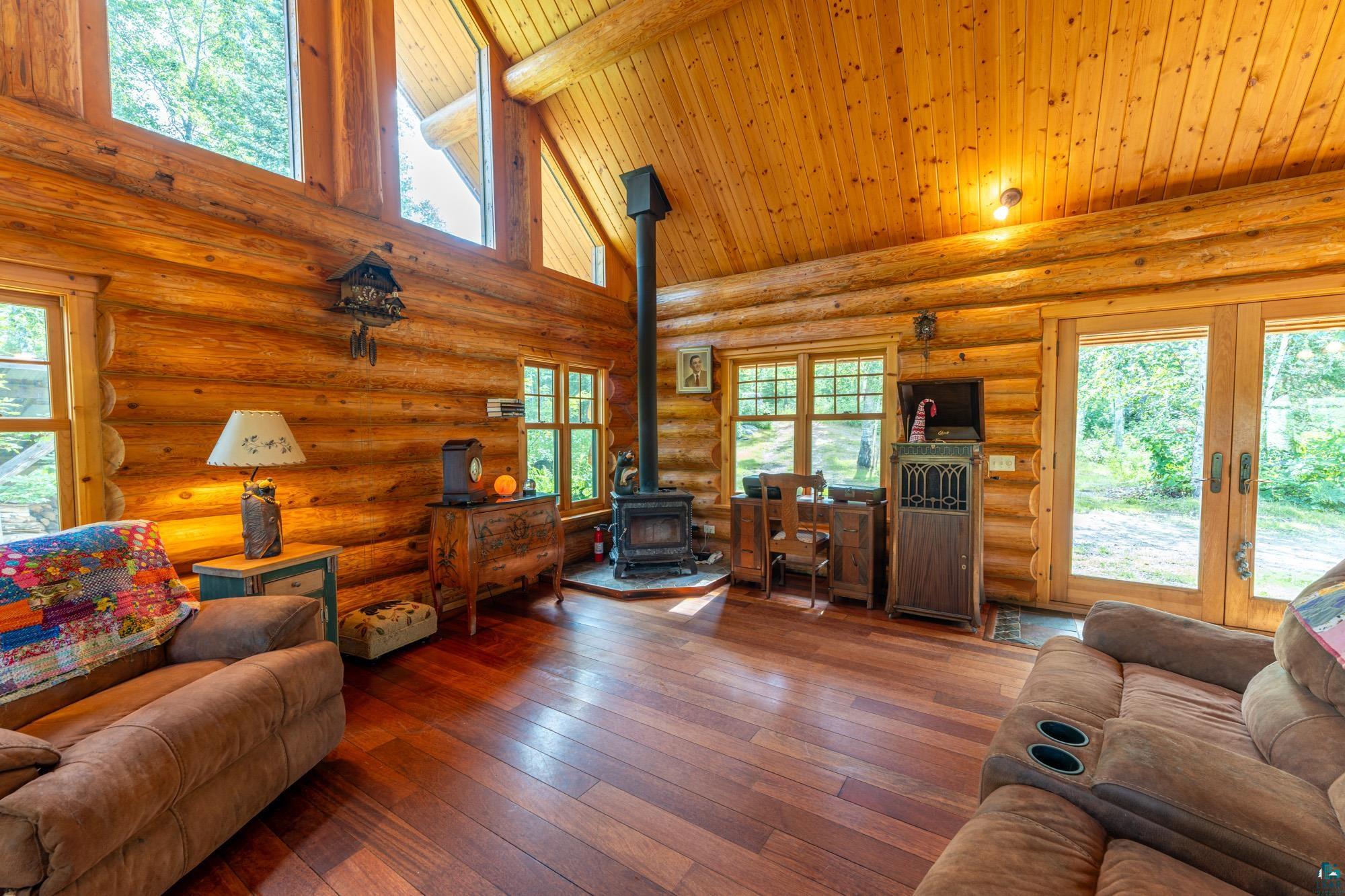 1911 Grouse Ridge Road Ely, MN 55731 - Photo 6 of 42 Living room with a wood stove, log walls, dark hardwood / wood-style floors, a healthy amount of sunlight, and high vaulted ceiling