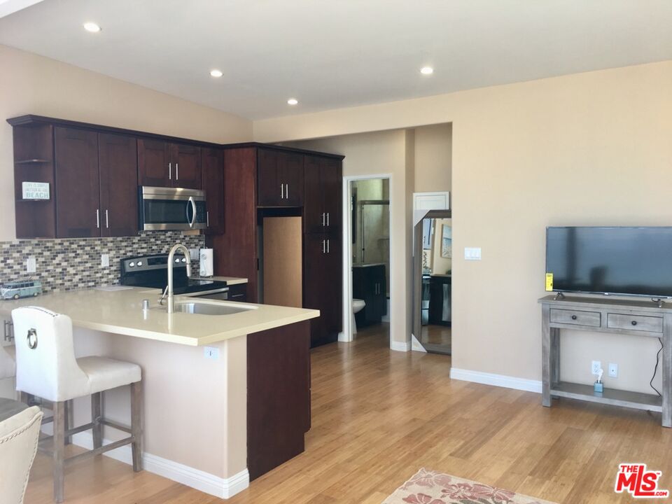 25164 Malibu Road, Unit D Malibu, CA 90265 - Photo 14 of 24 a kitchen with stainless steel appliances granite countertop a stove a refrigerator a sink a dining table and chairs with wooden floor
