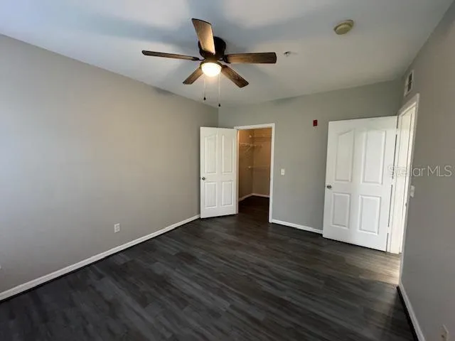a view of an empty room with wooden floor and a ceiling fan