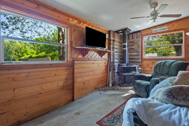 178 17th Street Ogden, UT 84404 - Photo 15 of 29 Room featuring wood paneling, a ceiling fan, and a freestanding wood-burning stove with a brick surround
